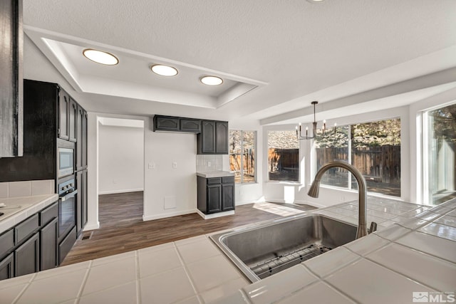 2510 Wolf Creek Dr, Reno, NV 89523 - kitchen featuring tile counters, a sink, a tray ceiling, dark wood-type flooring, and decorative backsplash