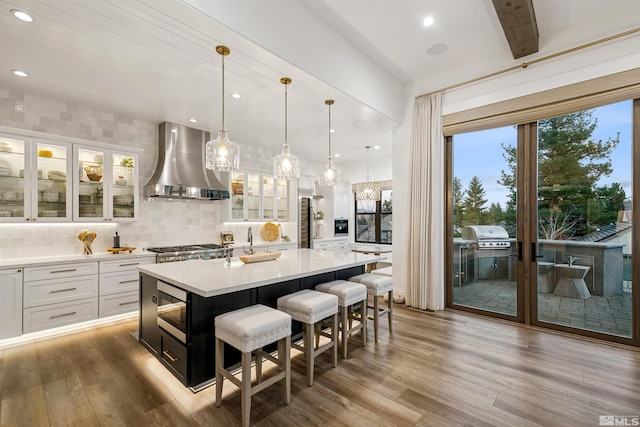 4312 Beaujolais St, Reno, NV 89511 - kitchen featuring wall chimney range hood, wood finished floors, white cabinets, stainless steel microwave, and a kitchen island with sink