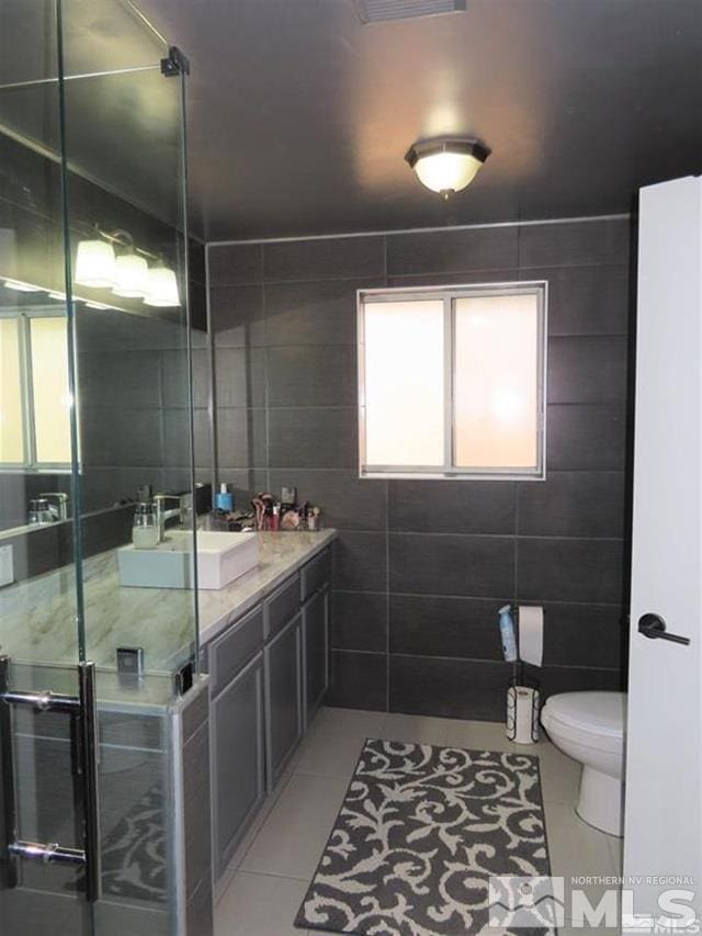 bathroom with tile patterned flooring, tile walls, toilet, a shower, and vanity