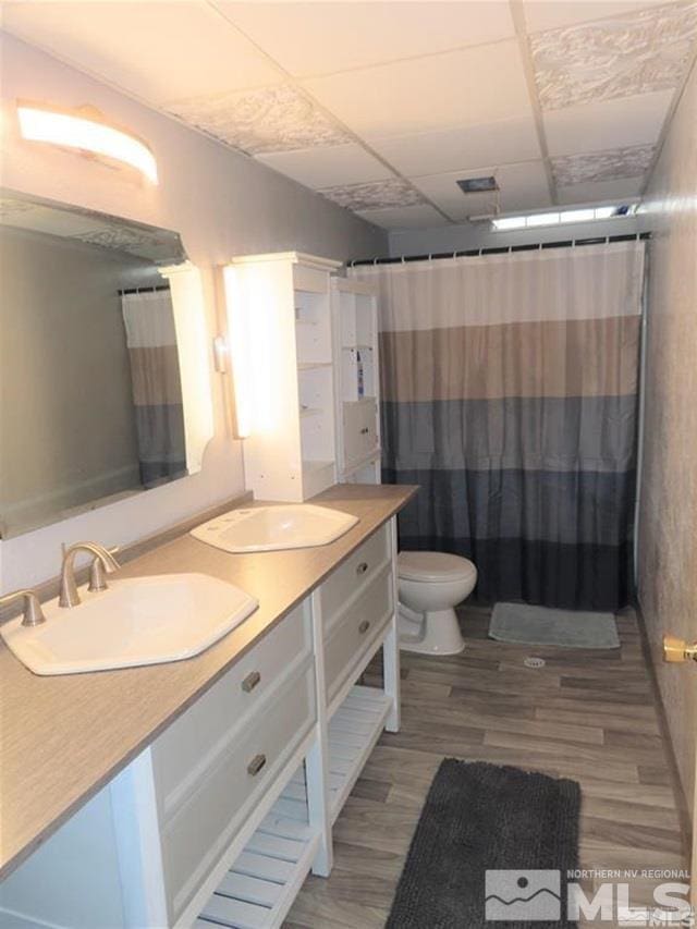 bathroom with double vanity, a paneled ceiling, toilet, wood finished floors, and curtained shower
