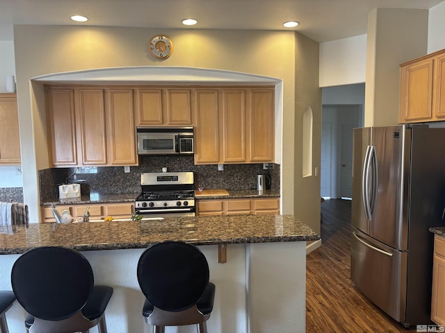 10316 Sterling View Ct, Reno, NV 89521 - kitchen featuring appliances with stainless steel finishes, dark wood-style flooring, dark stone countertops, backsplash, and a breakfast bar area