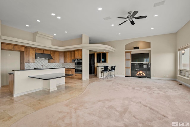 1150 Eagle Vista Ct, Reno, NV 89511 - kitchen with under cabinet range hood, brown cabinetry, open floor plan, stainless steel double oven, and recessed lighting
