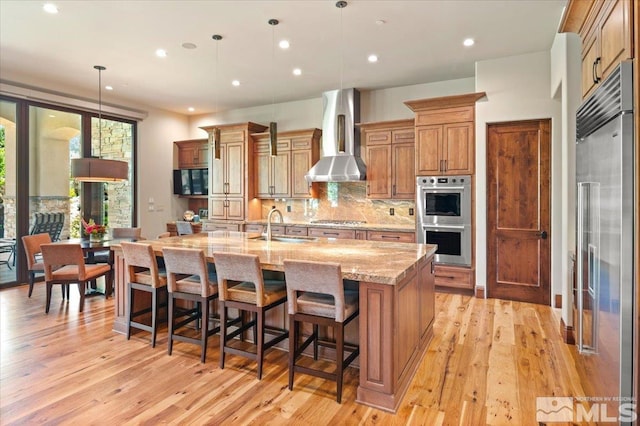 6645 De Chardin Ln, Reno, NV 89511 - kitchen with stainless steel appliances, a sink, wall chimney range hood, light wood-style floors, and a spacious island
