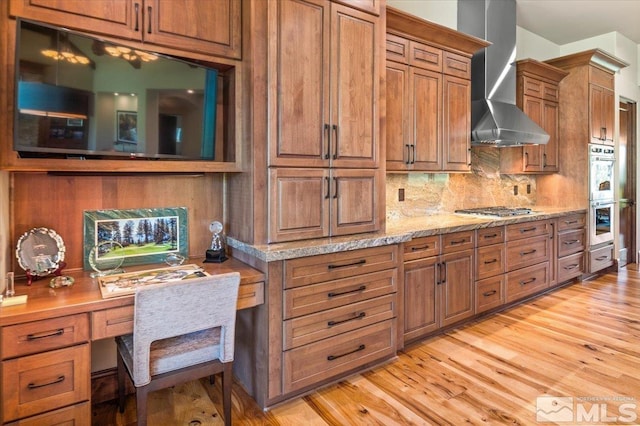 6645 De Chardin Ln, Reno, NV 89511 - kitchen featuring wall chimney range hood, stainless steel appliances, brown cabinetry, and light wood-style flooring