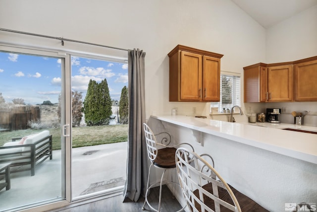 kitchen with high vaulted ceiling, brown cabinets, light countertops, wood finished floors, and a breakfast bar area