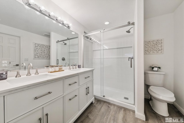 bathroom with wood finished floors, a stall shower, double vanity, and toilet