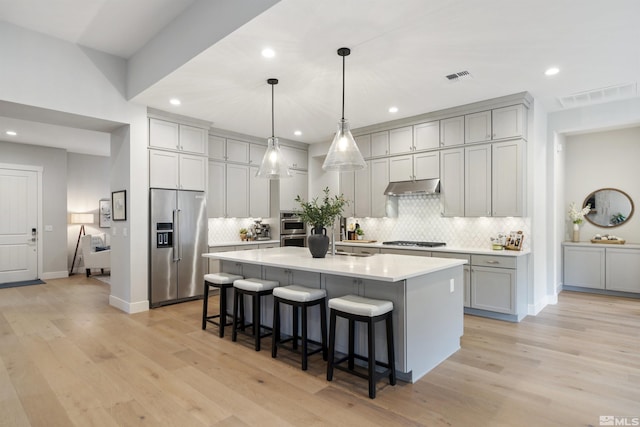 kitchen with stainless steel appliances, under cabinet range hood, gray cabinetry, a kitchen bar, and decorative backsplash