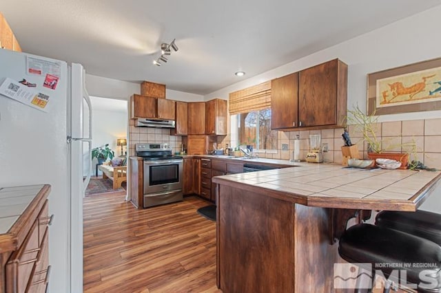 3920 W 7th St, Reno, NV 89503 - kitchen featuring stainless steel electric range oven, under cabinet range hood, freestanding refrigerator, tile countertops, and a peninsula