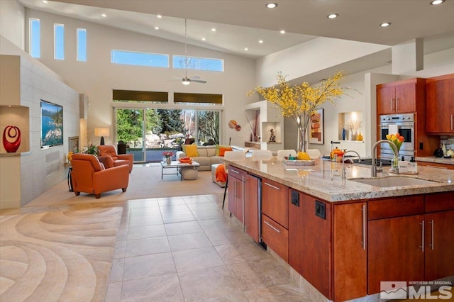 kitchen featuring a sink, open floor plan, recessed lighting, ceiling fan, and light stone counters
