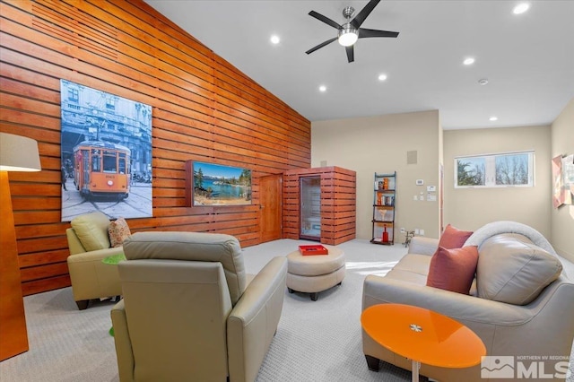 living area featuring vaulted ceiling, light colored carpet, wooden walls, recessed lighting, and a ceiling fan