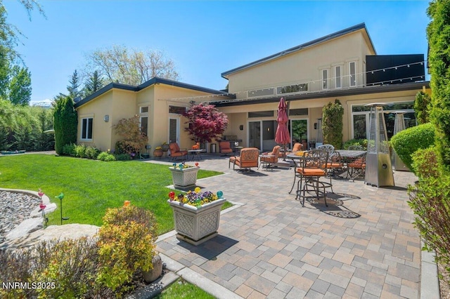 rear view of house with a lawn, a patio area, and stucco siding