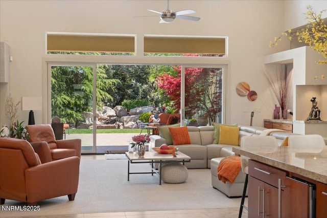 living area with ceiling fan, a towering ceiling, and light tile patterned floors