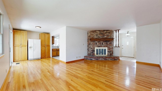 unfurnished living room with light wood-style flooring, a sink, plenty of natural light, and baseboards