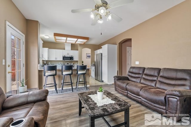 living area featuring arched walkways, ceiling fan, and light wood-type flooring