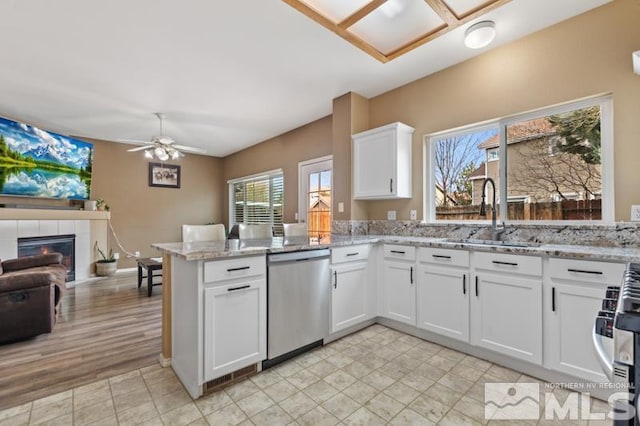 kitchen with dishwasher, a sink, a peninsula, ceiling fan, and white cabinetry