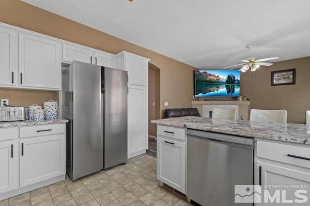 kitchen with appliances with stainless steel finishes, ceiling fan, white cabinetry, arched walkways, and light stone countertops