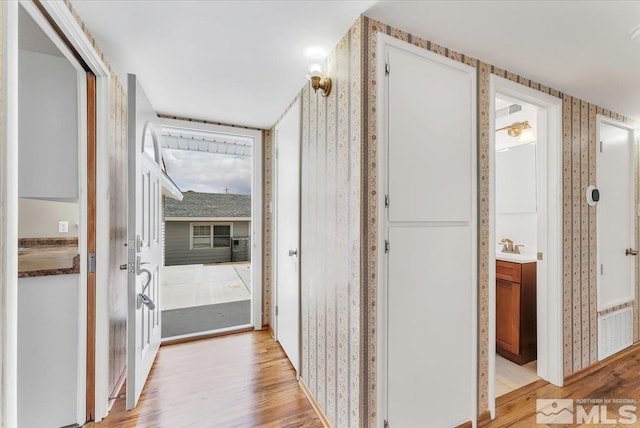 hall with wallpapered walls and light wood-style floors