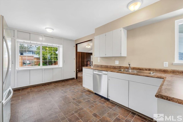 kitchen with appliances with stainless steel finishes, a sink, stone finish floors, and white cabinetry
