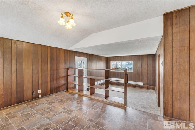 spare room featuring a textured ceiling, wood walls, a chandelier, stone finish flooring, and vaulted ceiling