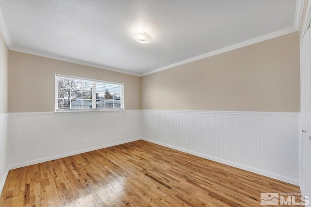 spare room featuring wood finished floors, wainscoting, crown molding, and baseboards