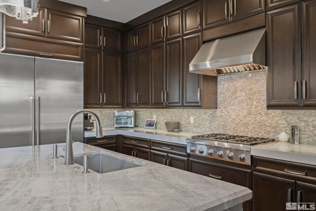 20588 Chanson Way, Reno, NV 89511 - kitchen with wall chimney range hood, appliances with stainless steel finishes, a sink, dark brown cabinets, and decorative backsplash