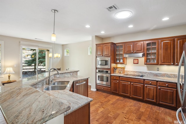 kitchen featuring appliances with stainless steel finishes, a sink, under cabinet range hood, a spacious island, and light wood-style floors