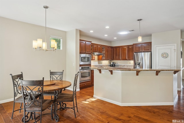 kitchen featuring appliances with stainless steel finishes, under cabinet range hood, a kitchen bar, a chandelier, and dark wood-style floors