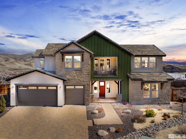 view of front facade with a balcony, stone siding, driveway, board and batten siding, and a garage