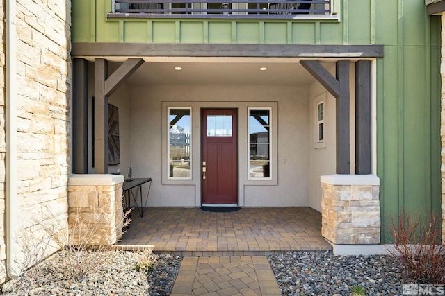 doorway to property with stone siding, board and batten siding, and a balcony