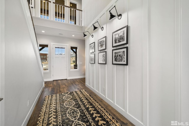 entryway with wood finished floors, baseboards, and a towering ceiling
