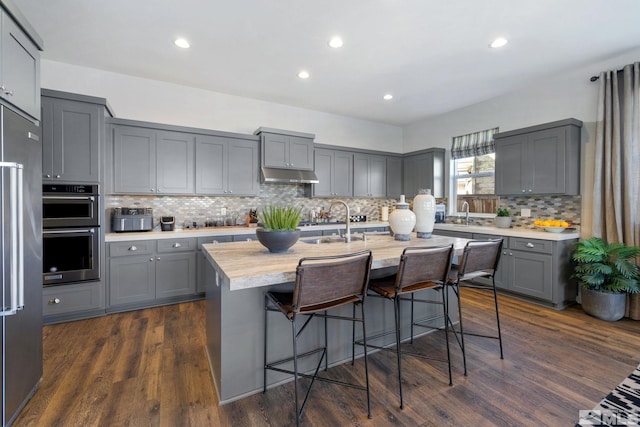 kitchen with gray cabinets, under cabinet range hood, appliances with stainless steel finishes, light countertops, and recessed lighting