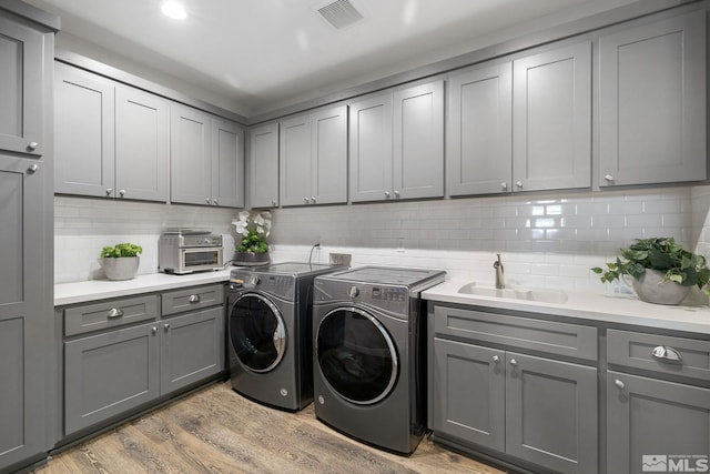 clothes washing area with a sink, washing machine and dryer, and light wood-style flooring