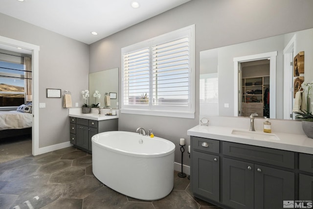 full bathroom with baseboards, ensuite bath, a freestanding bath, stone finish flooring, and two vanities