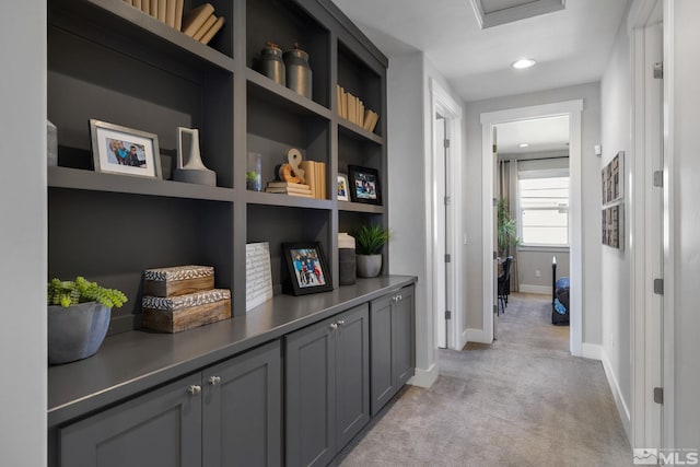 hallway featuring light carpet, baseboards, and attic access
