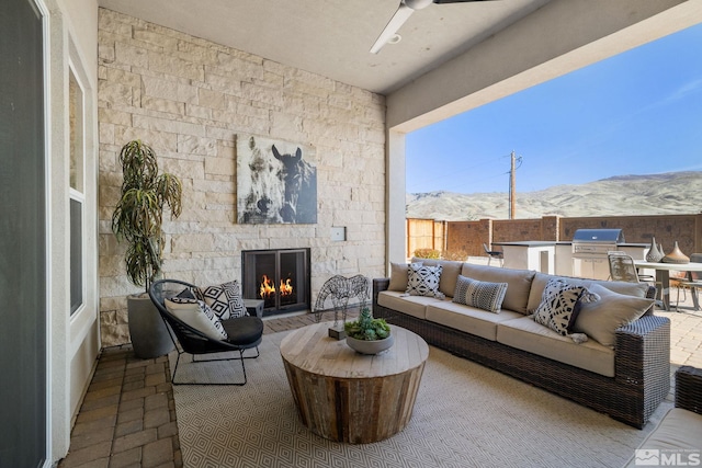 view of patio featuring an outdoor kitchen, an outdoor living space with a fireplace, grilling area, a mountain view, and fence