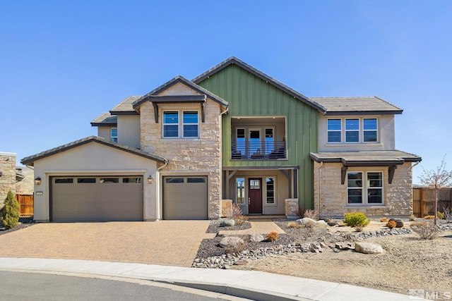 craftsman house featuring stone siding, fence, decorative driveway, a balcony, and board and batten siding
