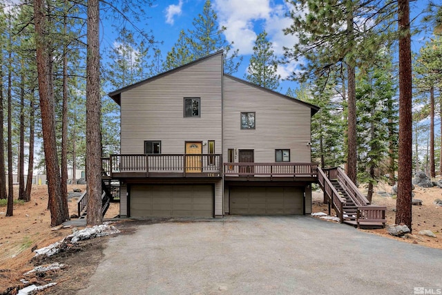back of house featuring stairway, a deck, asphalt driveway, and an attached garage