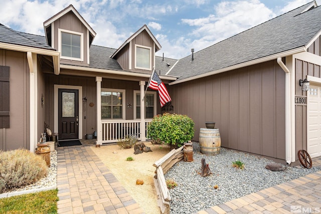 entrance to property with a porch, a shingled roof, a garage, and board and batten siding