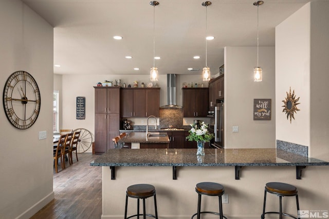 kitchen with wall chimney range hood, high end refrigerator, dark wood-type flooring, dark brown cabinets, and decorative backsplash