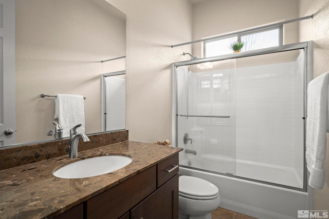 full bath with bath / shower combo with glass door, vanity, a textured wall, and toilet