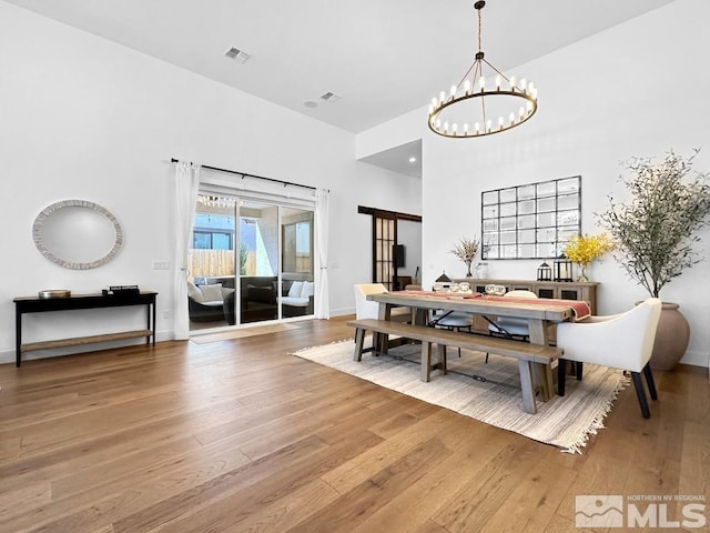 dining space featuring a chandelier, wood-type flooring, a high ceiling, and baseboards