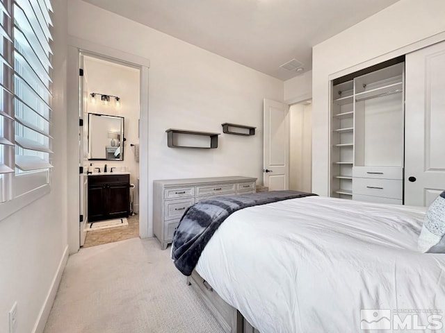 bedroom featuring light carpet, a closet, ensuite bath, a sink, and baseboards
