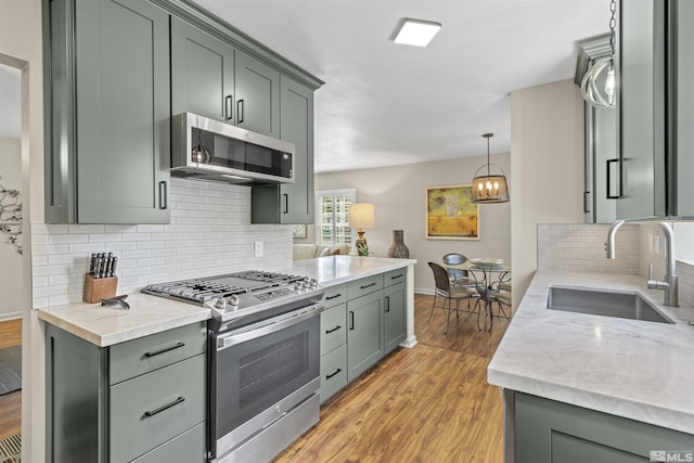 823 Arbutus St, Reno, NV 89509 - kitchen with appliances with stainless steel finishes, a sink, light wood finished floors, green cabinetry, and backsplash