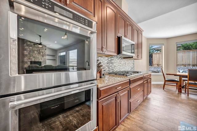 16885 Majestic View Dr, Reno, NV 89521 - kitchen featuring appliances with stainless steel finishes, ceiling fan, light wood finished floors, decorative backsplash, and a fireplace