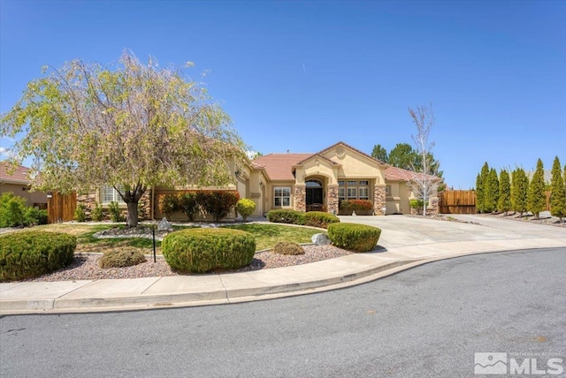 mediterranean / spanish-style home featuring stone siding, stucco siding, curved driveway, fence, and a tile roof