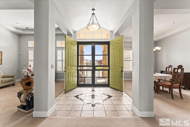foyer featuring light carpet, baseboards, lofted ceiling, light tile patterned flooring, and a chandelier
