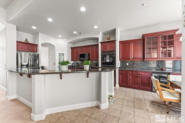 kitchen with reddish brown cabinets, appliances with stainless steel finishes, decorative backsplash, wine cooler, and arched walkways
