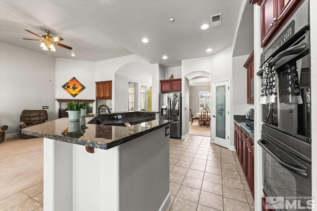 kitchen featuring stainless steel refrigerator with ice dispenser, a sink, open floor plan, dark brown cabinets, and arched walkways