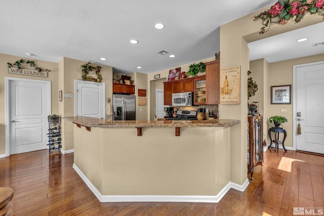 kitchen featuring stainless steel appliances, brown cabinets, dark wood-type flooring, baseboards, and recessed lighting