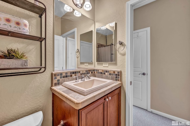 bathroom featuring toilet, a textured wall, vanity, and decorative backsplash
